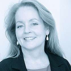 A woman with long hair, wearing earrings and a blazer, smiling at the camera.
