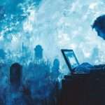 A person sits at a laptop in a cemetery, surrounded by tombstones, with a glowing blue sky in the background.