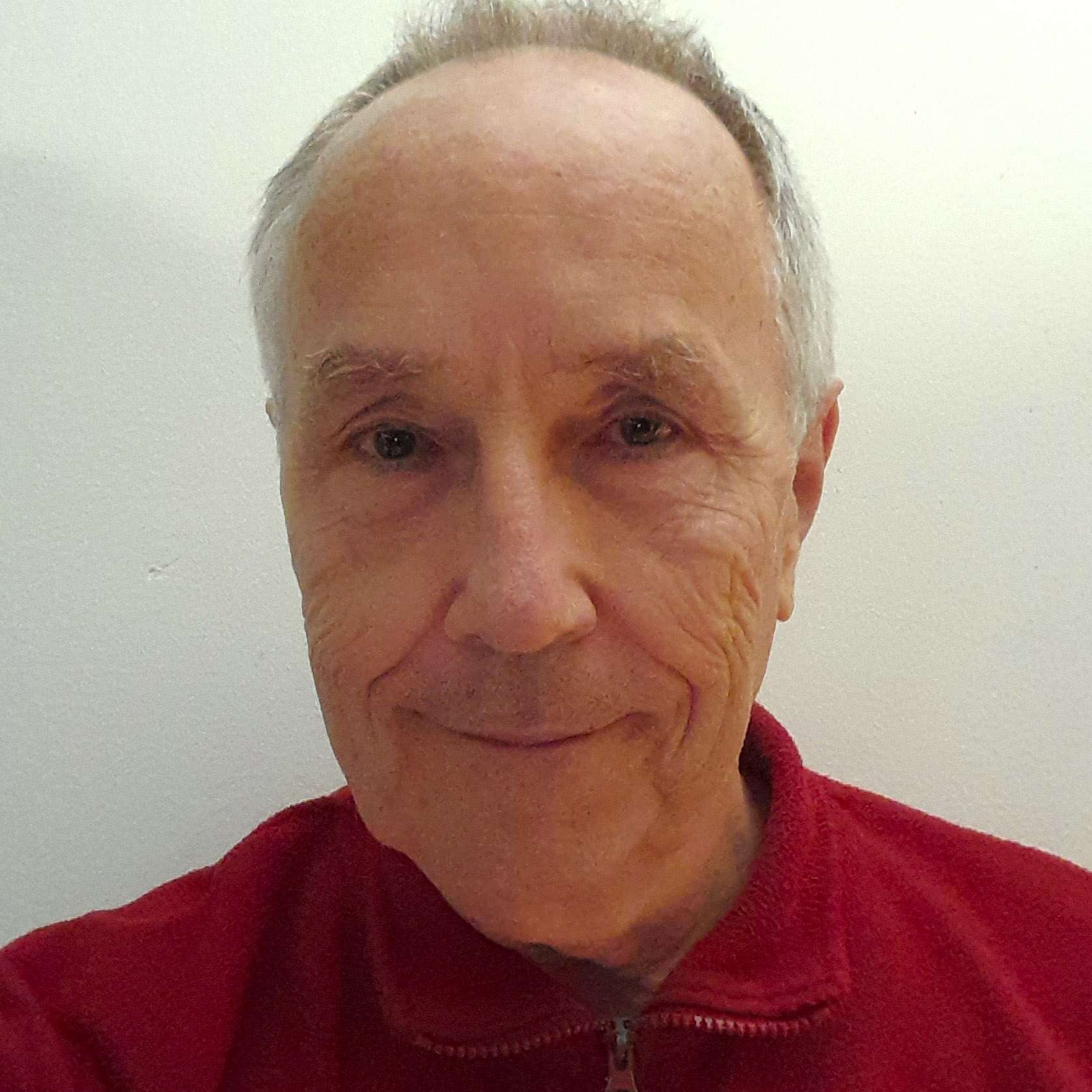 A man wearing a red sweater smiles at the camera against a plain white background.