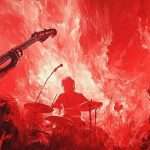 Silhouetted rock band performs with intense red light and flames in the background.