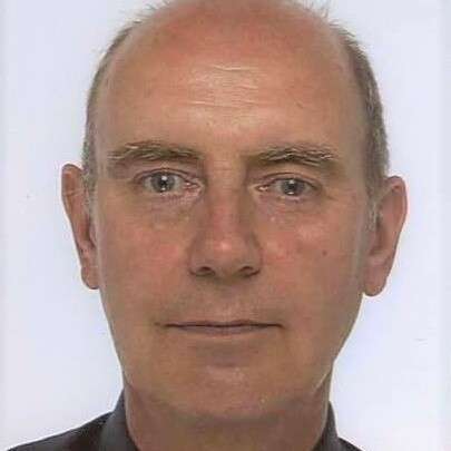 A bald man with a neutral expression looks directly at the camera in a close-up portrait against a plain background.