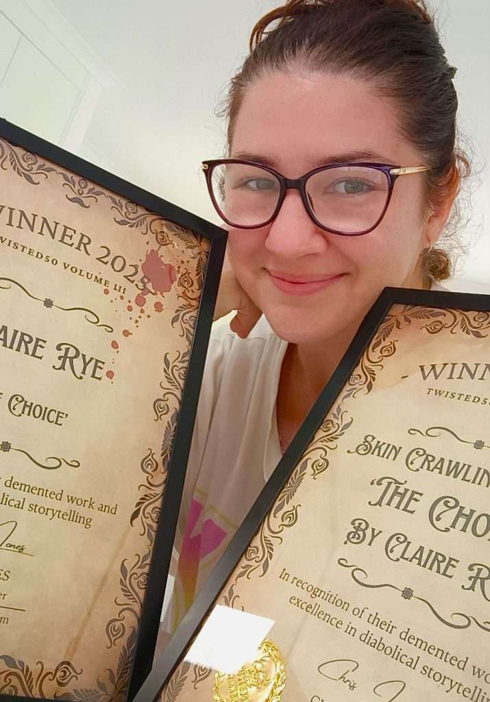 A person holding two award certificates, smiling at the camera. The certificates are framed and feature decorative text.